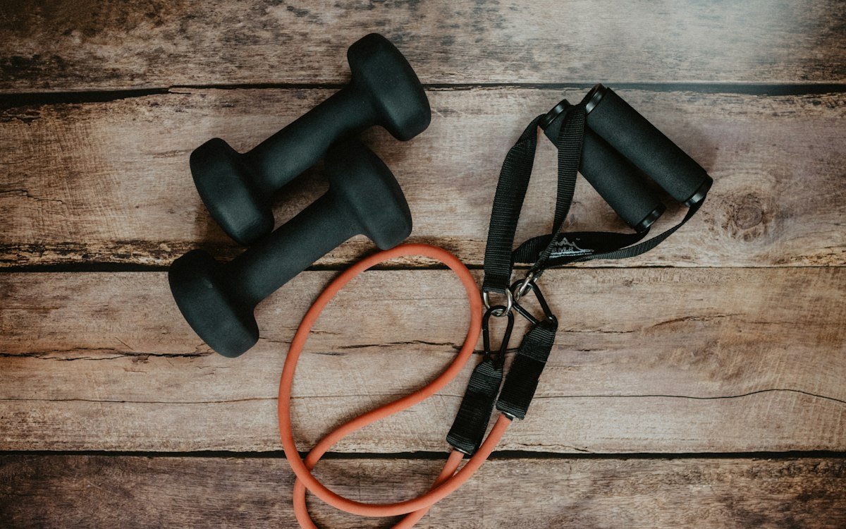 Two black dumbbells and an orange resistance band on a rustic wooden surface